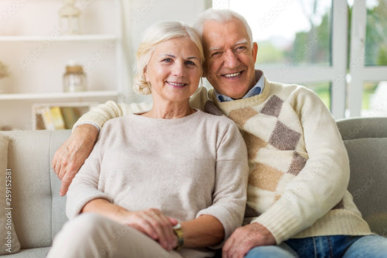 senior couple in their living room sitting on a sofa holding each other around their shoulders and smiling