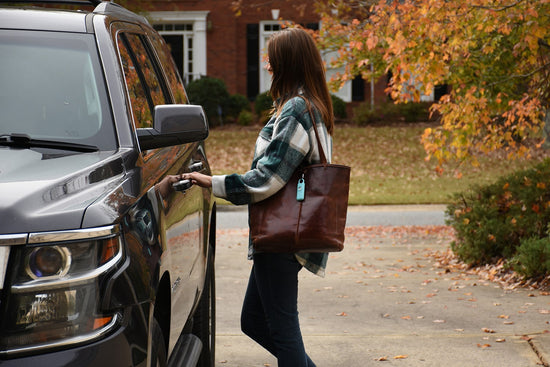a fifty year old woman with long brown hair carrying brown leather tote with attached personal safety siren opening her car