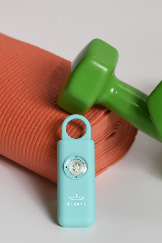 safety device for women with strobing led light laying on a rolled up orange yoga mat and green dumb bell